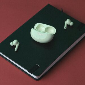 Green notebook and wireless earbuds on red surface, perfect for technology-themed still life.