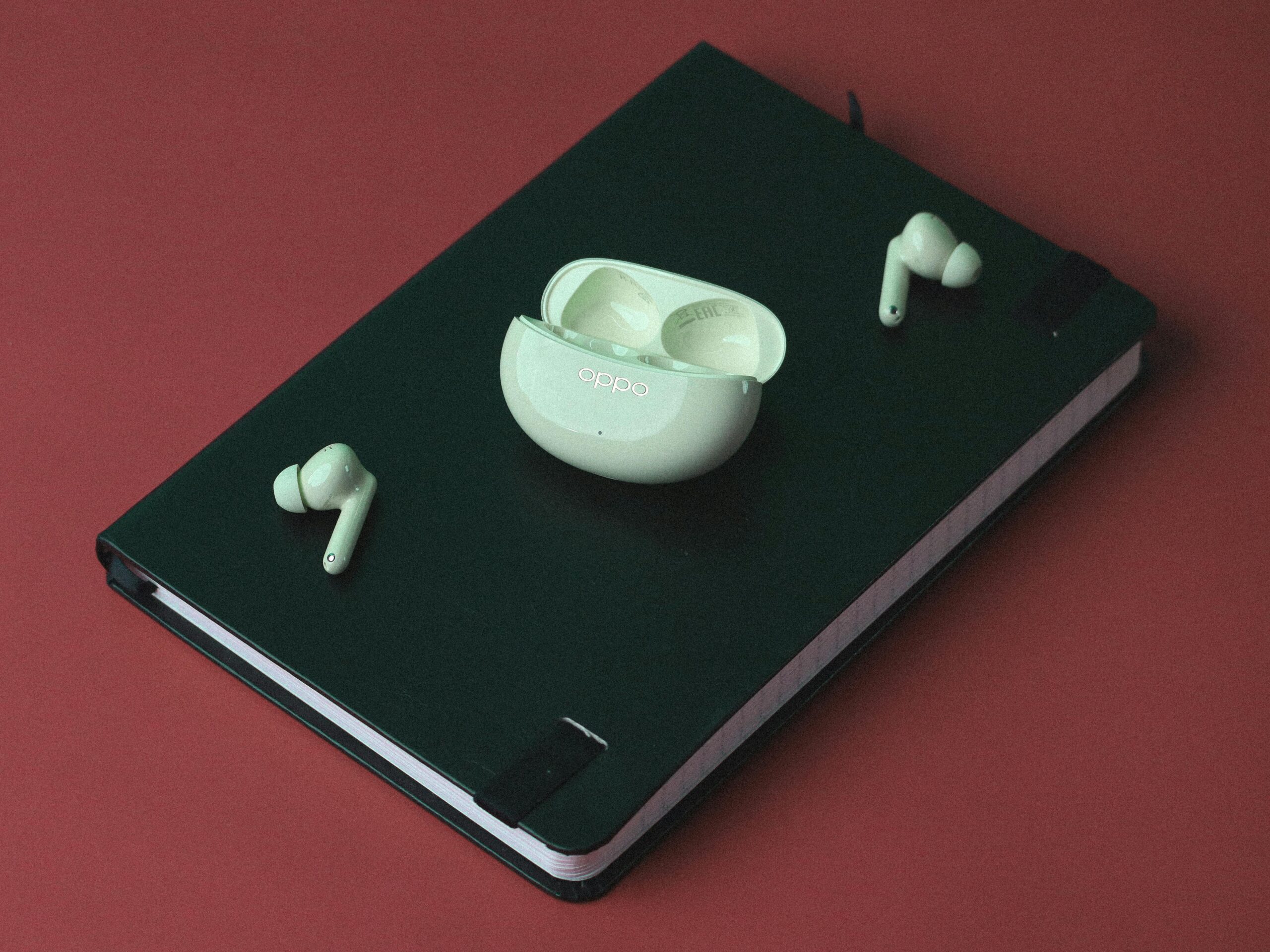 Green notebook and wireless earbuds on red surface, perfect for technology-themed still life.